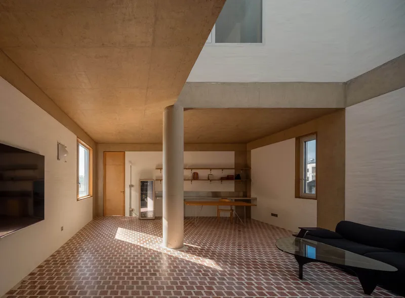 Open living area with cylindrical column and timber ceiling panels illuminated by afternoon sunlight