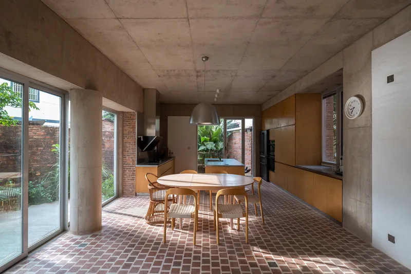 Open-plan kitchen and dining area with exposed concrete ceiling and terracotta tile floor under afternoon sunlight