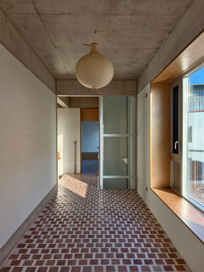 Circulation hallway with terracotta herringbone floor and spherical pendant light beneath concrete ceiling