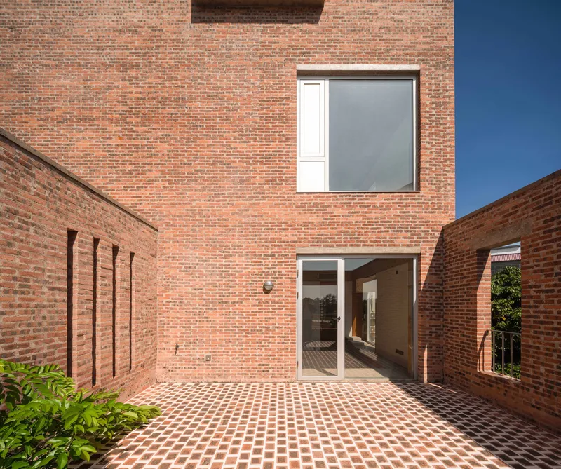 Brick courtyard with chequered paving leading to glass doors under a square window with partial screening