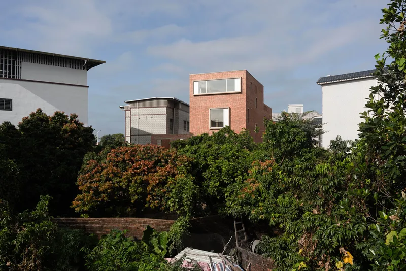 Brick mass with staggered openings emerging above dense foliage and a lower retaining wall