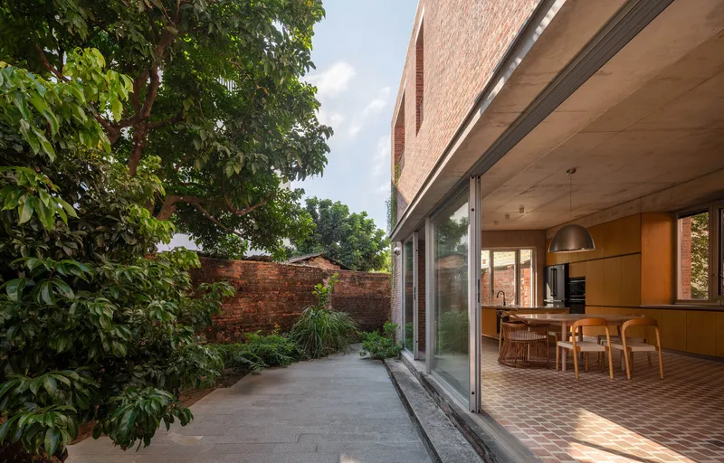 Full-height glazing opening from dining area to courtyard terrace with tree canopy overhead