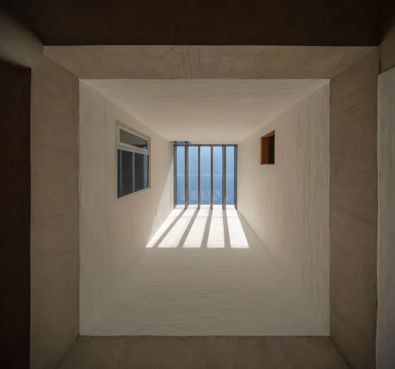 Looking up through a skylight shaft with vertical louvers casting striped shadows on white plaster walls