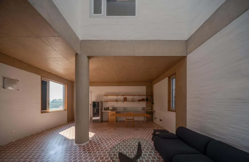 Open-plan interior with cylindrical column separating living area from kitchen with timber dining table