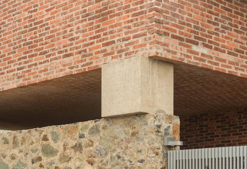 Detail of concrete column meeting red brick wall and stone foundation beneath timber soffit