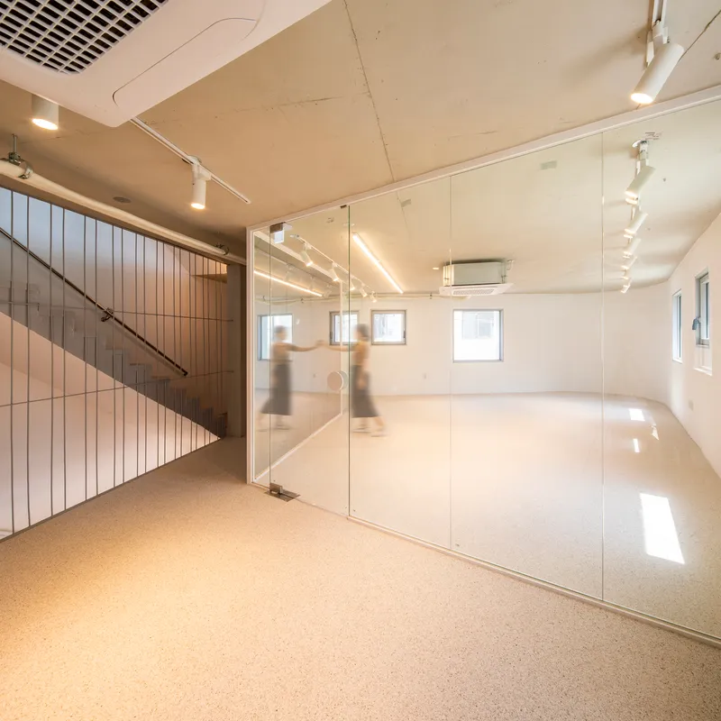 Interior space with glass partition, exposed plywood ceiling, track lighting, and blurred figures moving near the stairwell