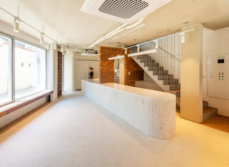 Ground floor entry hall with curved white-tiled reception desk, exposed brick wall, and metal staircase with cable railings