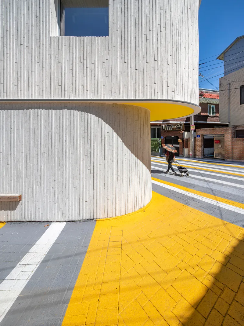 Close-up of the curving white facade underside painted bright yellow, sheltering the yellow-paved sidewalk with a pedestrian passing