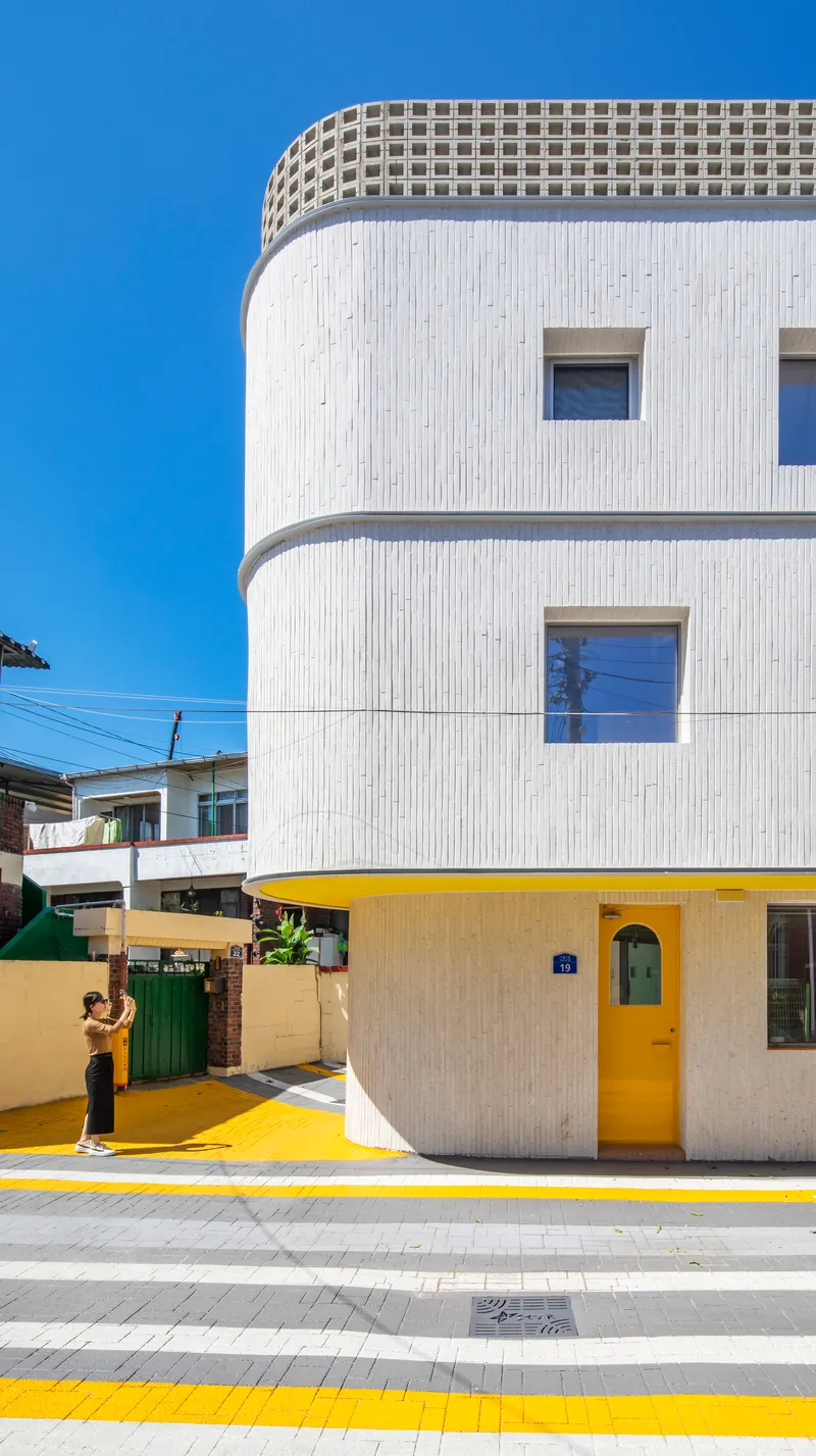 Street view of the white cylindrical tower with yellow door and crosswalk as a person approaches