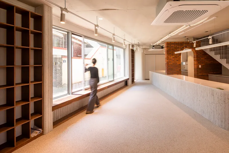 Interior ground floor with ribbed counter, exposed brick wall, and figure walking past the window