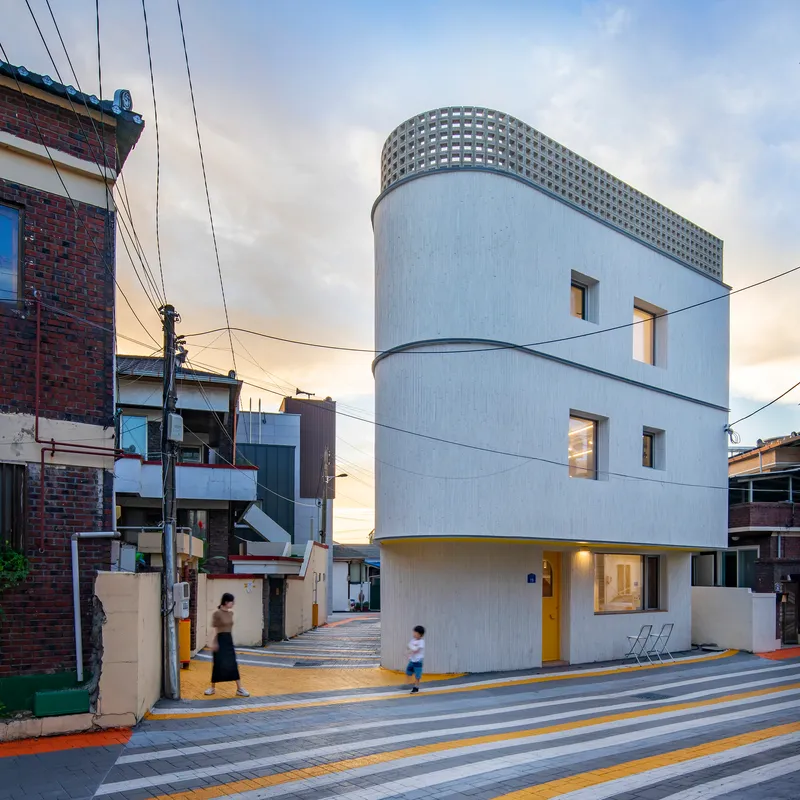 Curved white facade with perforated parapet at the corner of a striped pedestrian crosswalk at dusk