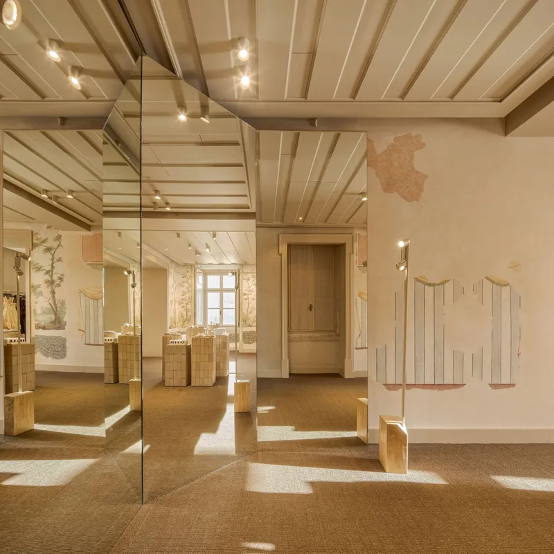 Interior gallery with exposed timber ceiling beams, mirrored columns and sunlight streaming across cork flooring