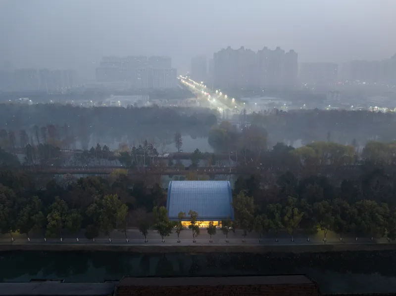 Aerial view of the arched roof structure nestled among trees with misty towers in the distance