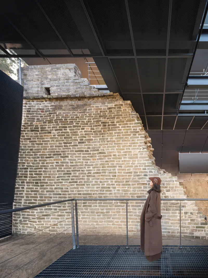 Visitor standing on walkway alongside preserved brick wall with visible deterioration and openings