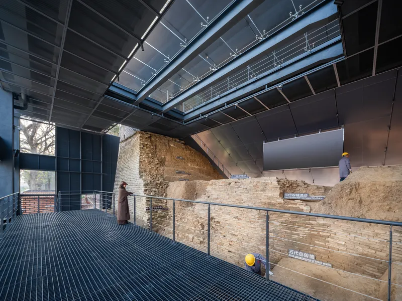 Interior gallery showing exposed earthen rampart strata with metal railings and visitors on perforated floor decking