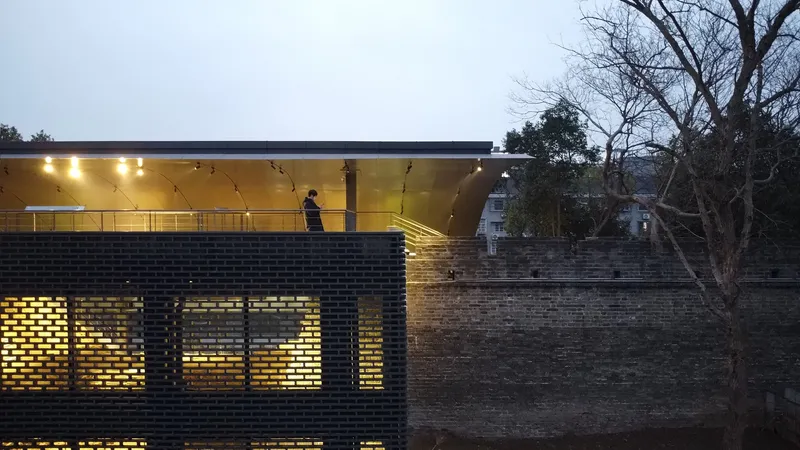 Nighttime view of the perforated brick facade with backlit openings and visitor on upper canopy level