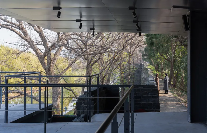 Covered walkway with steel railings framing view of brick ruins among bare trees