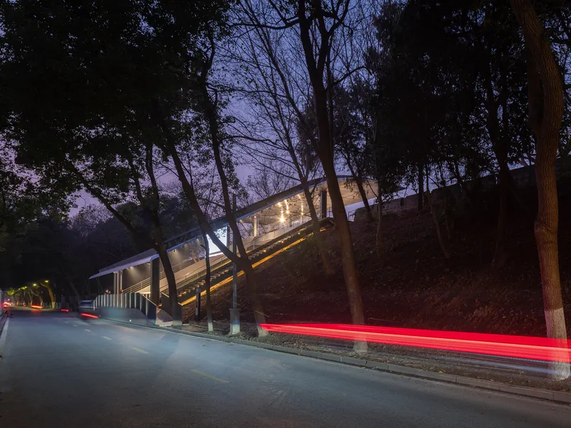 Street view of the illuminated structure against wooded hillside with car light trails passing at night