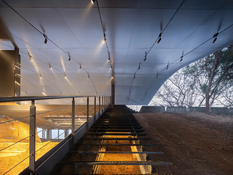 Timber staircase with metal mesh railings descends beneath a paneled ceiling with track lighting at dusk