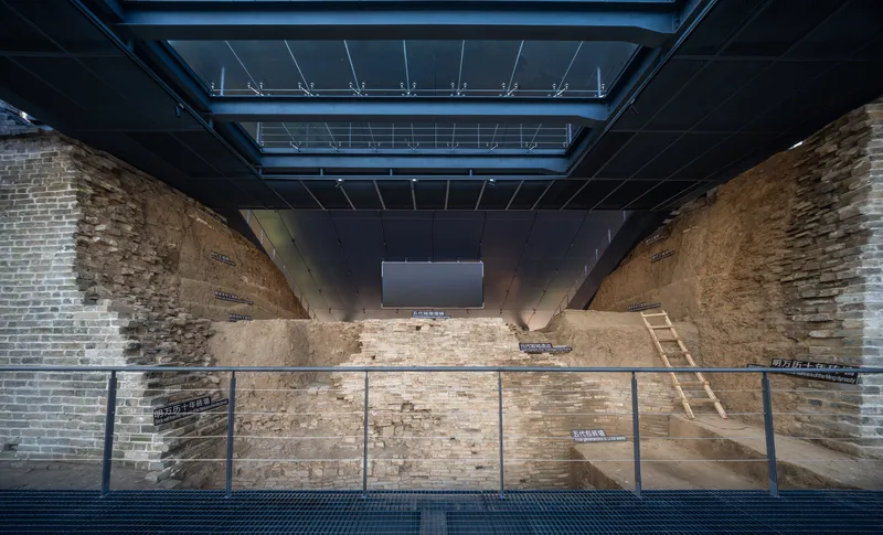 Excavated brick foundation walls beneath a steel and glass ceiling with overhead skylights