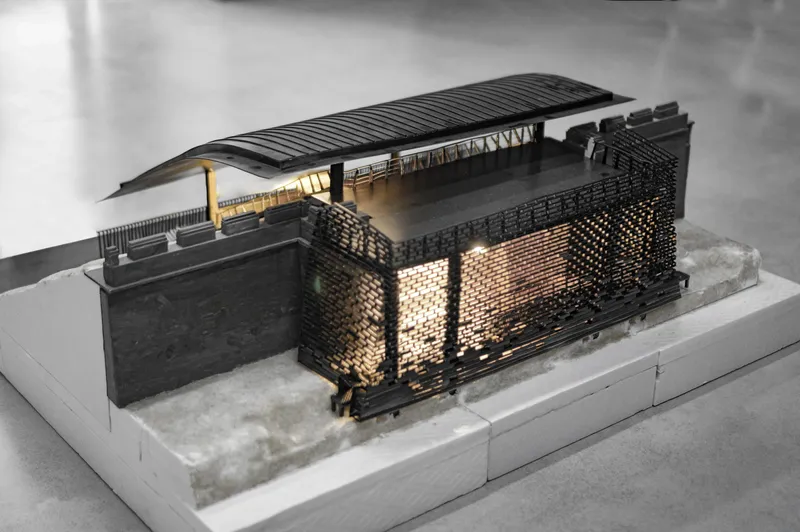 Physical model with perforated brick screen walls and a ribbed arched roof under warm interior lighting