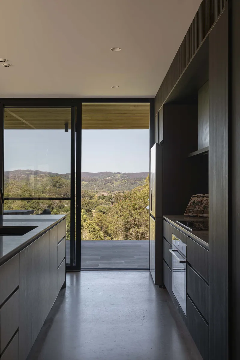 Kitchen corridor with dark cabinetry and full-height glazing opening to the terrace and bushland beyond