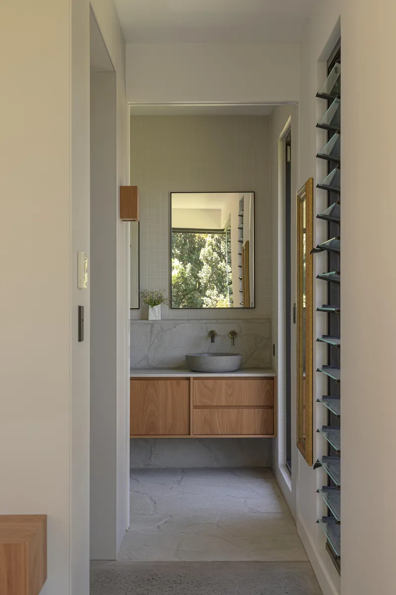 Hallway view into bathroom with concrete floor, timber vanity, and framed window with tree foliage outside