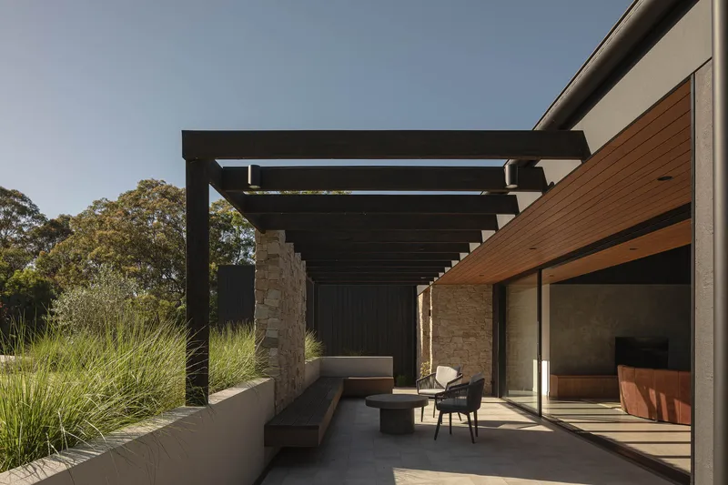 Covered terrace with dark timber pergola and stone walls under afternoon sun