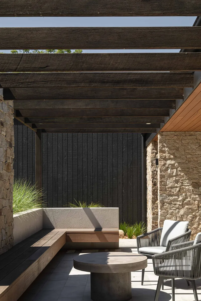 Pergola seating area with timber beams casting shadows on concrete paving below