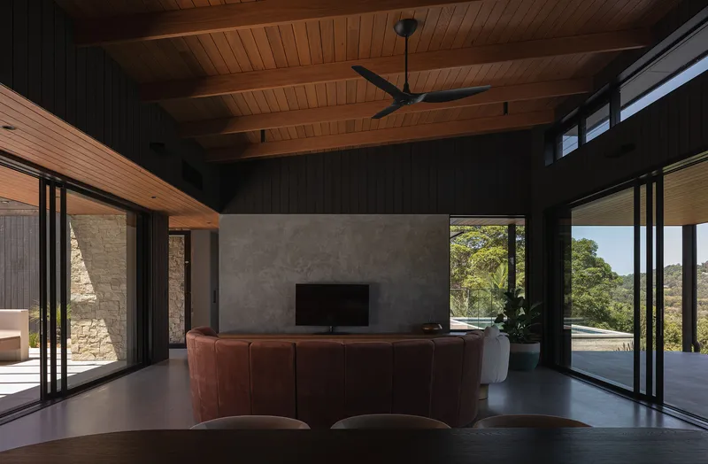 Living room with concrete fireplace wall and timber-lined ceiling opening to the pool terrace