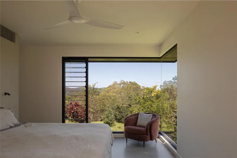 Bedroom corner window framing distant hills and garden vegetation in afternoon light