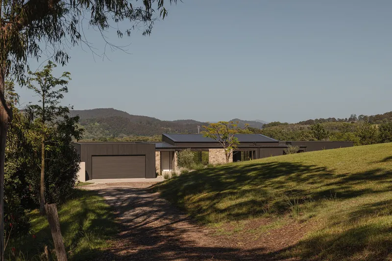 Long view of the horizontal residence nestled on a grassy hillside with eucalyptus trees and distant mountains