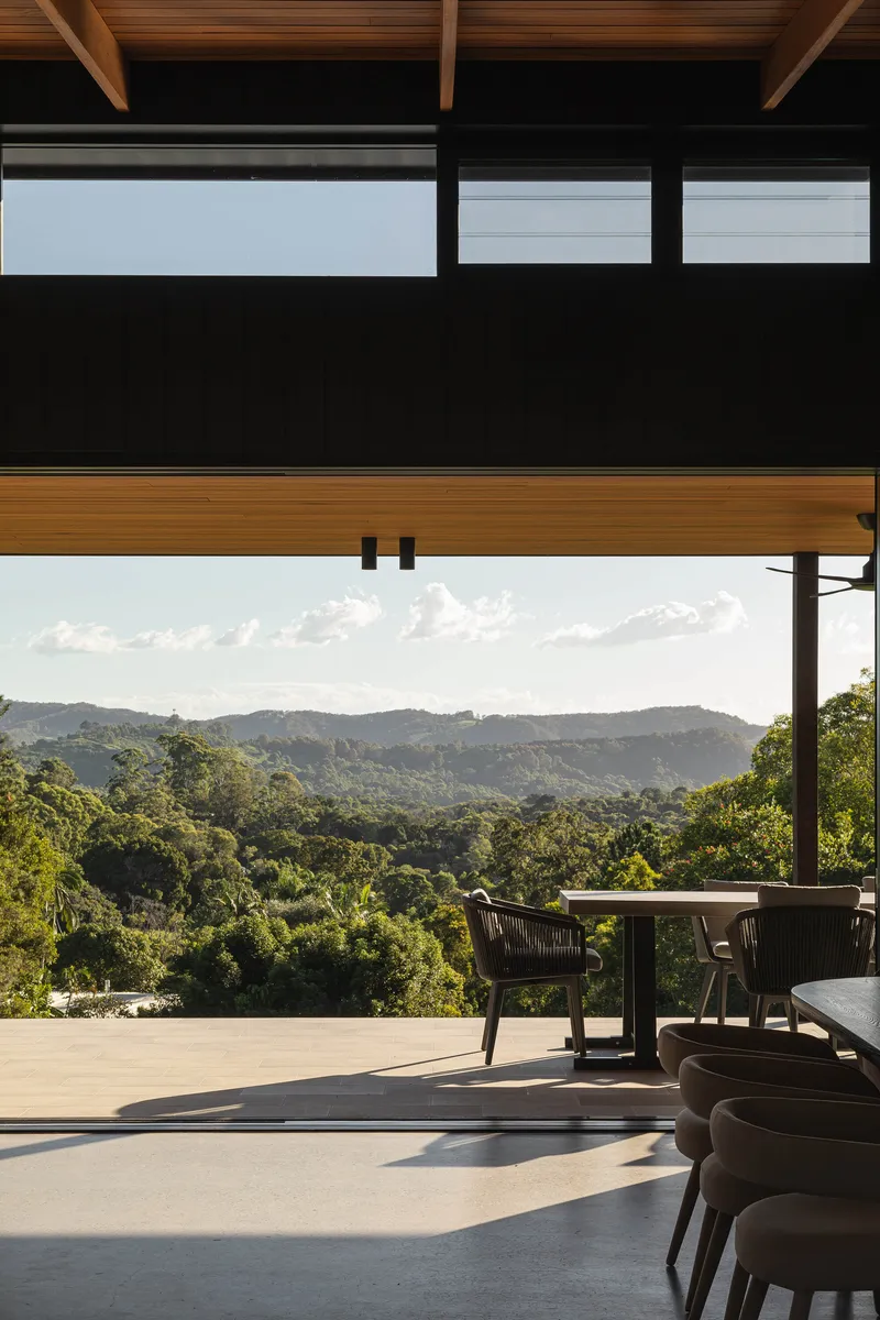 Covered outdoor dining terrace with timber rafters overlooking forested hills at dusk