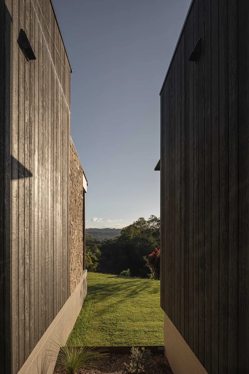 Narrow passage between vertical timber cladding and stone walls opening to lawn