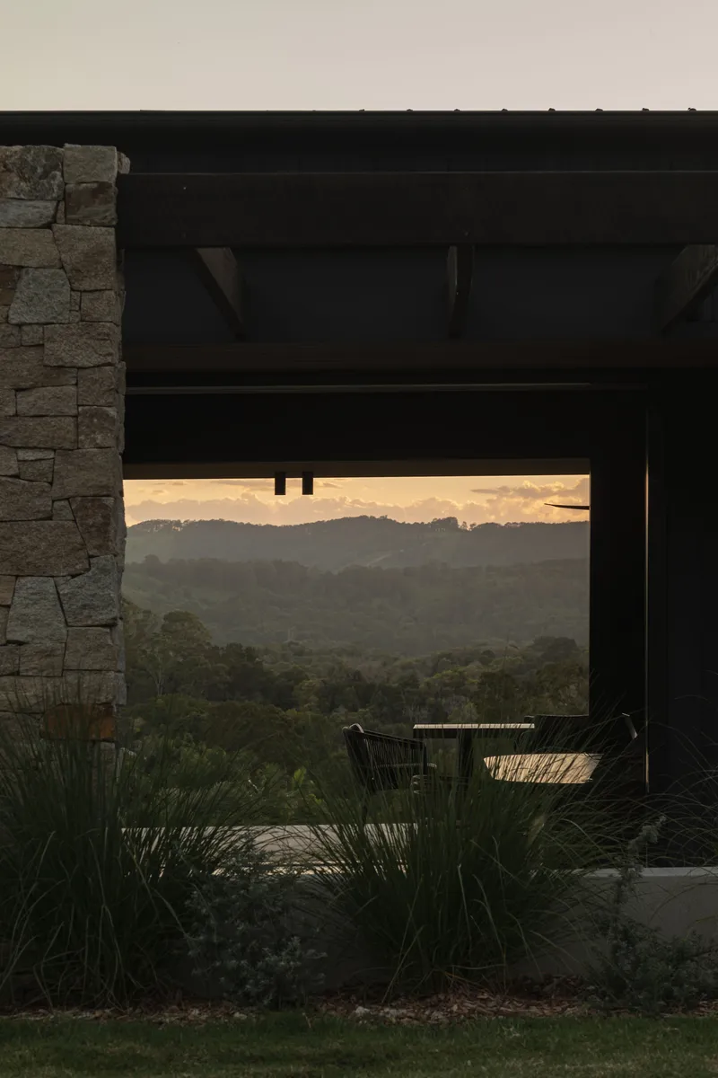 View through the covered terrace with stacked stone wall framing distant hills at dusk