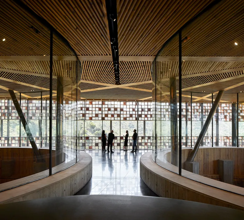 Central hall with ribbed timber ceiling, curved balconies and visitors silhouetted against perforated screens