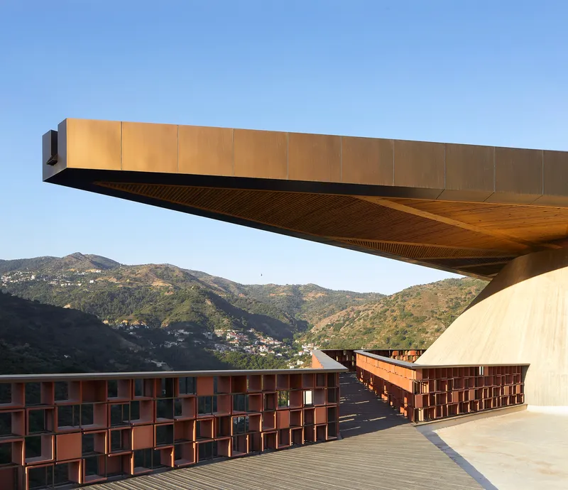 Cantilevered roof overhang with timber soffit above copper-clad volumes and terraced courtyard