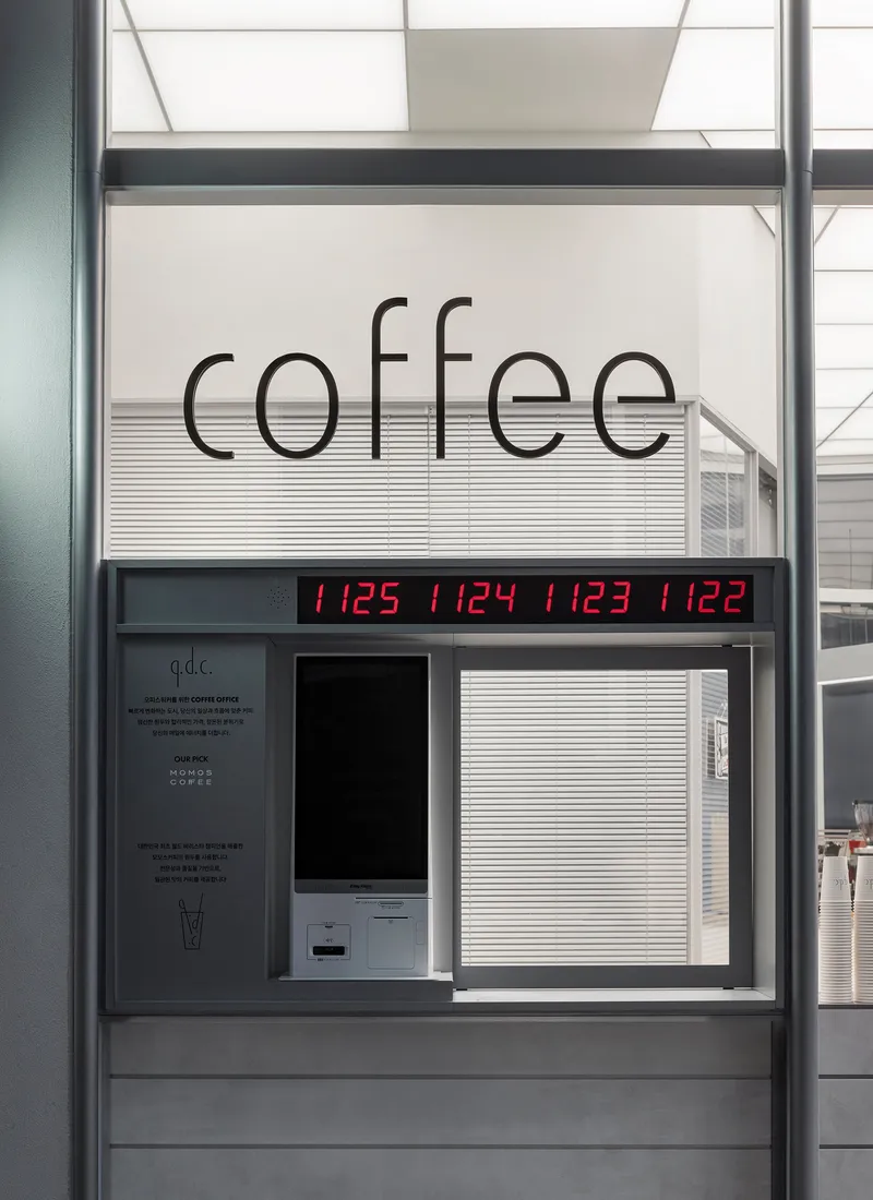 Service window with digital time display and automated ordering kiosk below coffee signage