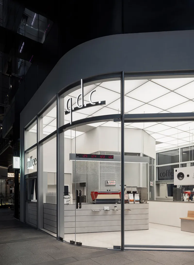 Glass storefront with curved white ceiling and horizontal slatted counter in a shadowed arcade