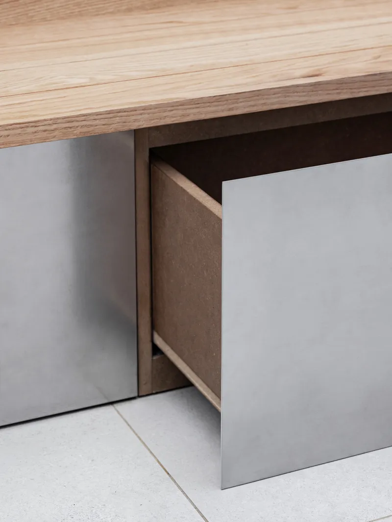 Detail of open drawer beneath wooden countertop with gray laminate base cabinet