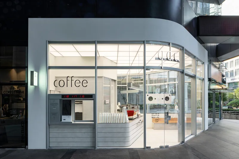 Curved glass storefront with horizontal ribbed counter beneath illuminated grid ceiling at dusk