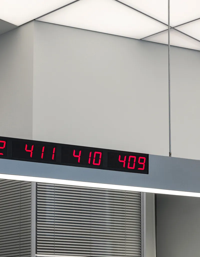 Red digital number display mounted on gray ceiling soffit above horizontal louvers