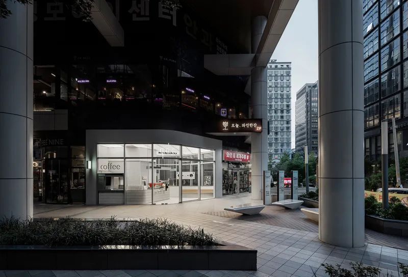 Curved glass facade of the retail kiosk nestled between cylindrical columns in the evening