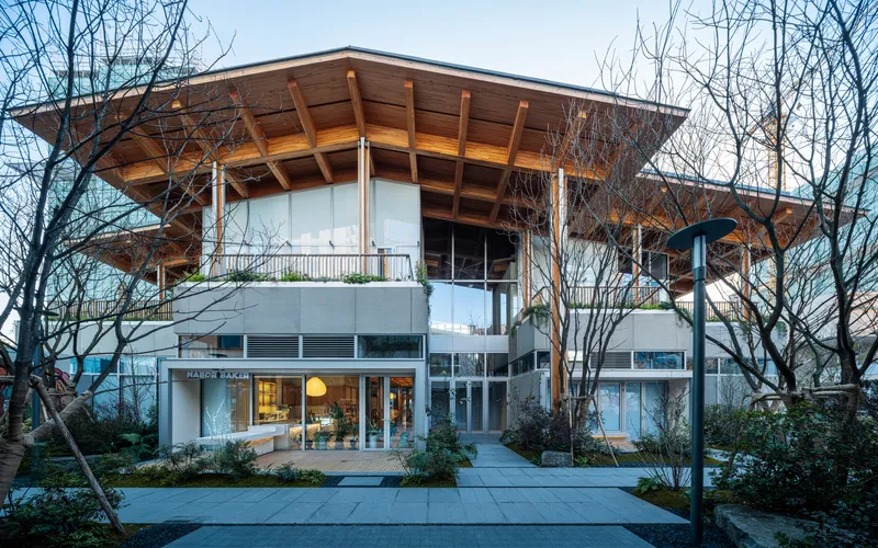 Two-story facade with overhanging timber roof and exposed rafters framed by bare winter trees at dusk