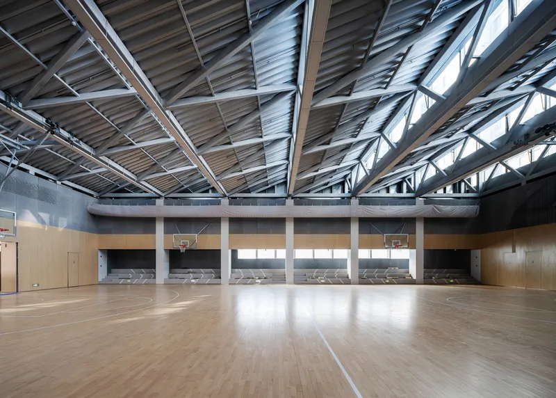 Gymnasium interior with timber floor, basketball hoops and exposed steel truss ceiling with clerestory windows