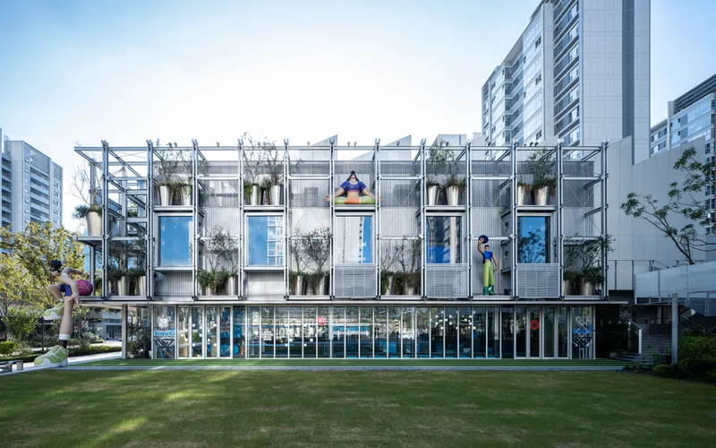 Front elevation of steel-framed structure with modular units and hanging plants viewed across a sunlit lawn