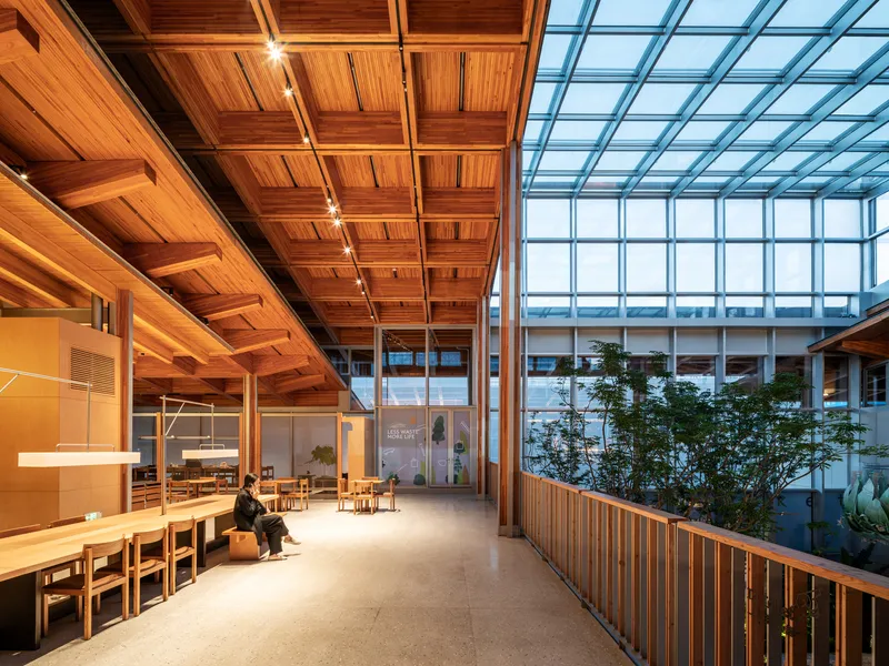 Interior corridor with coffered timber ceiling and central glass atrium with planted trees at dusk