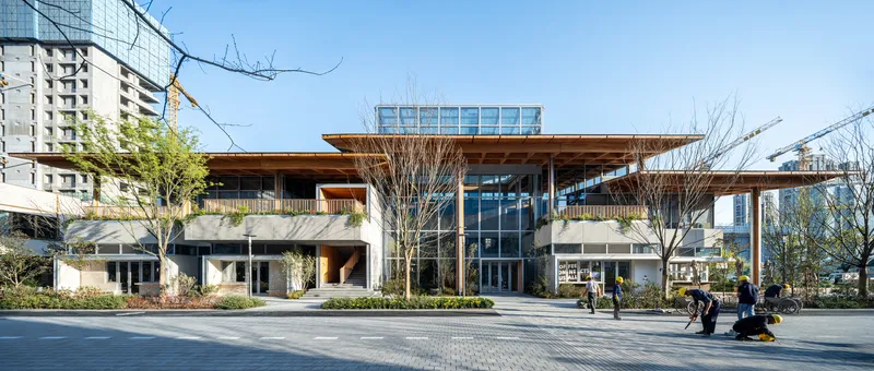 Street elevation showing timber roof overhang and central glass atrium with pedestrians in plaza