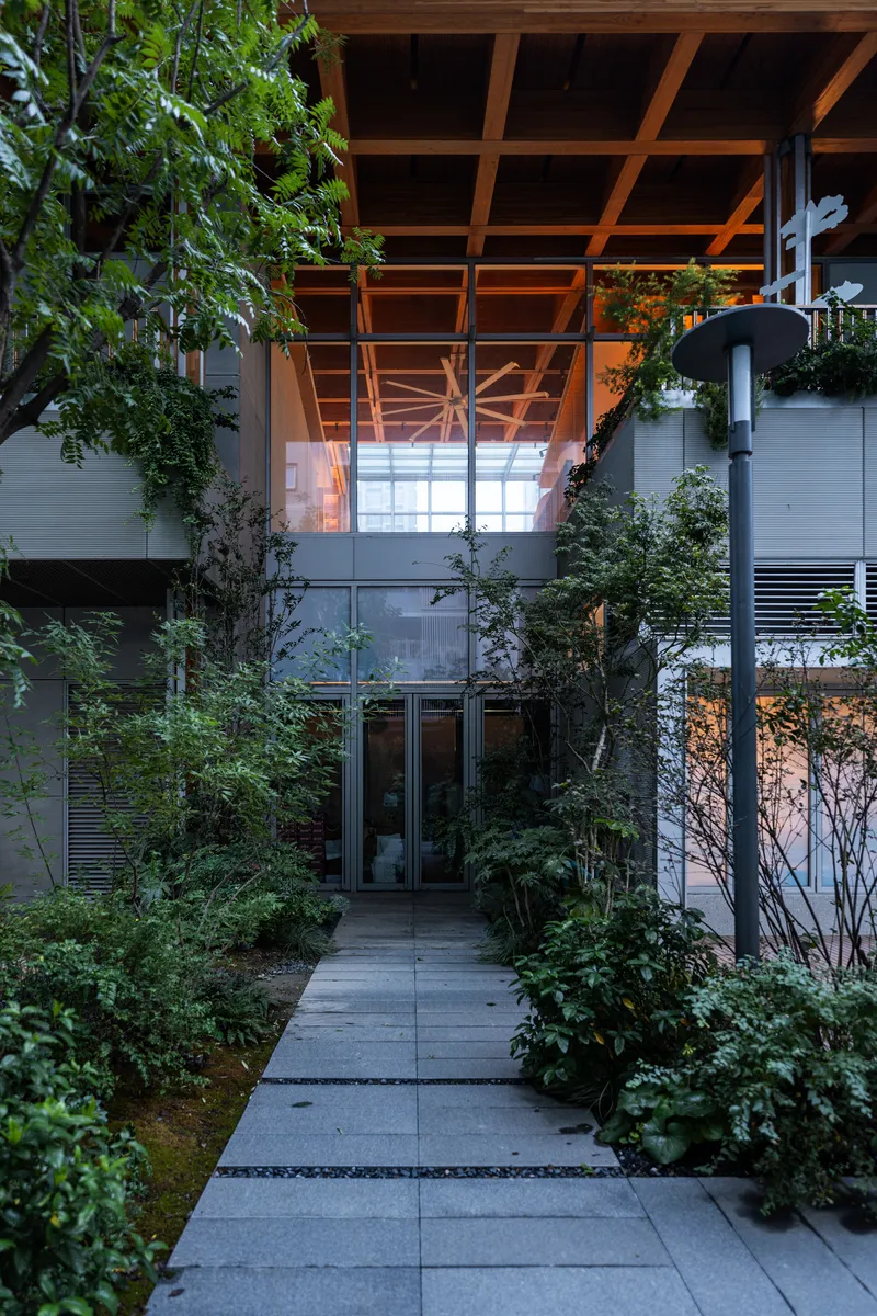 Entry path lined with planted beds leading to glass doors beneath the cantilevering timber-beam roof at dusk