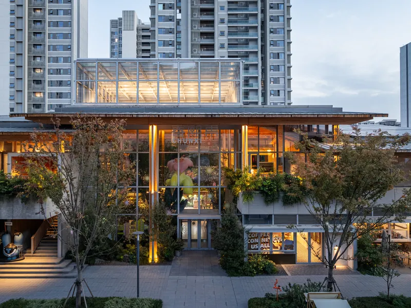 Glass-enclosed upper pavilion with exposed timber structure illuminated at dusk with residential towers beyond